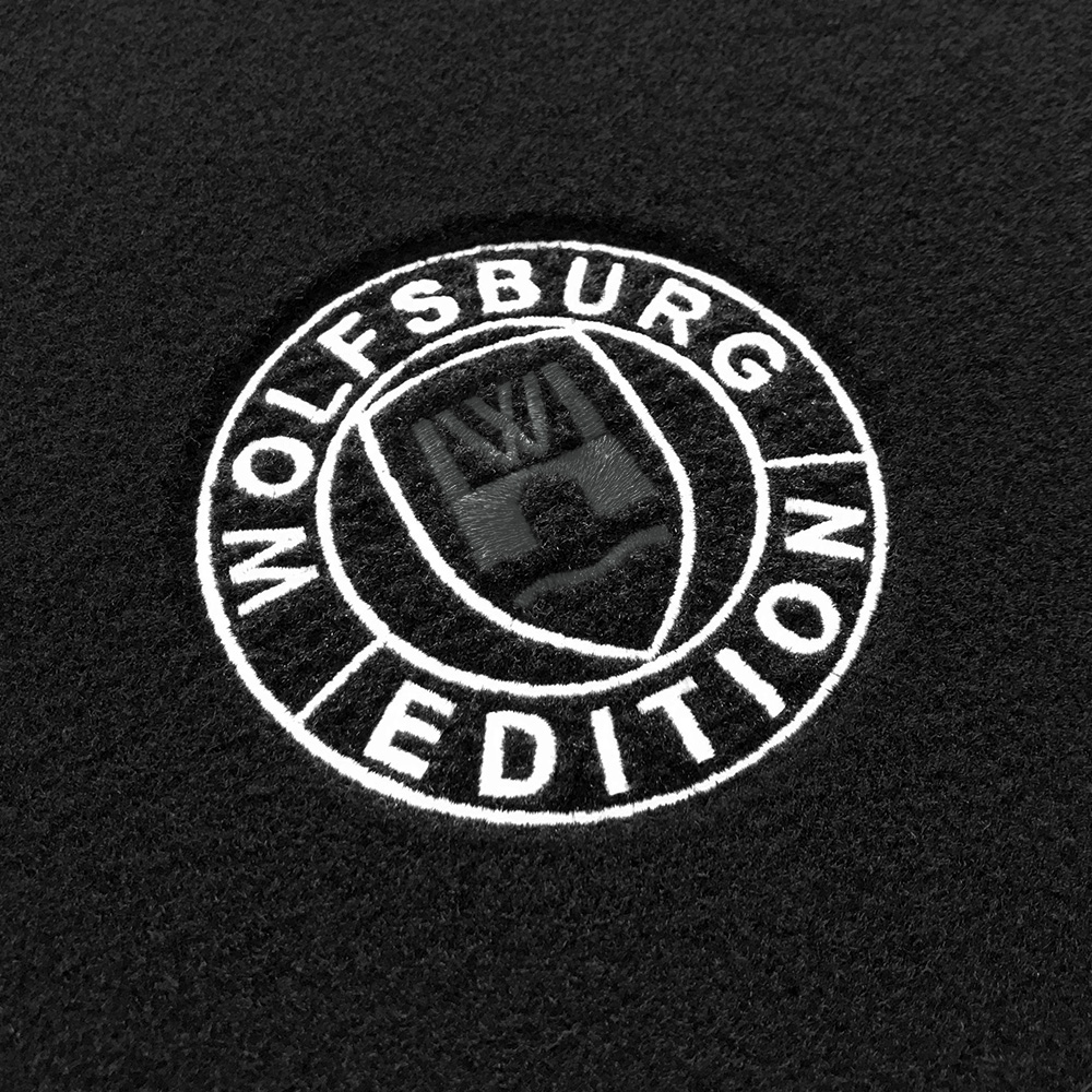 Das gestickte Wolfsburg Editions Logo auf einem schwarzen Teppich und das Logo ist in anthrazit.
