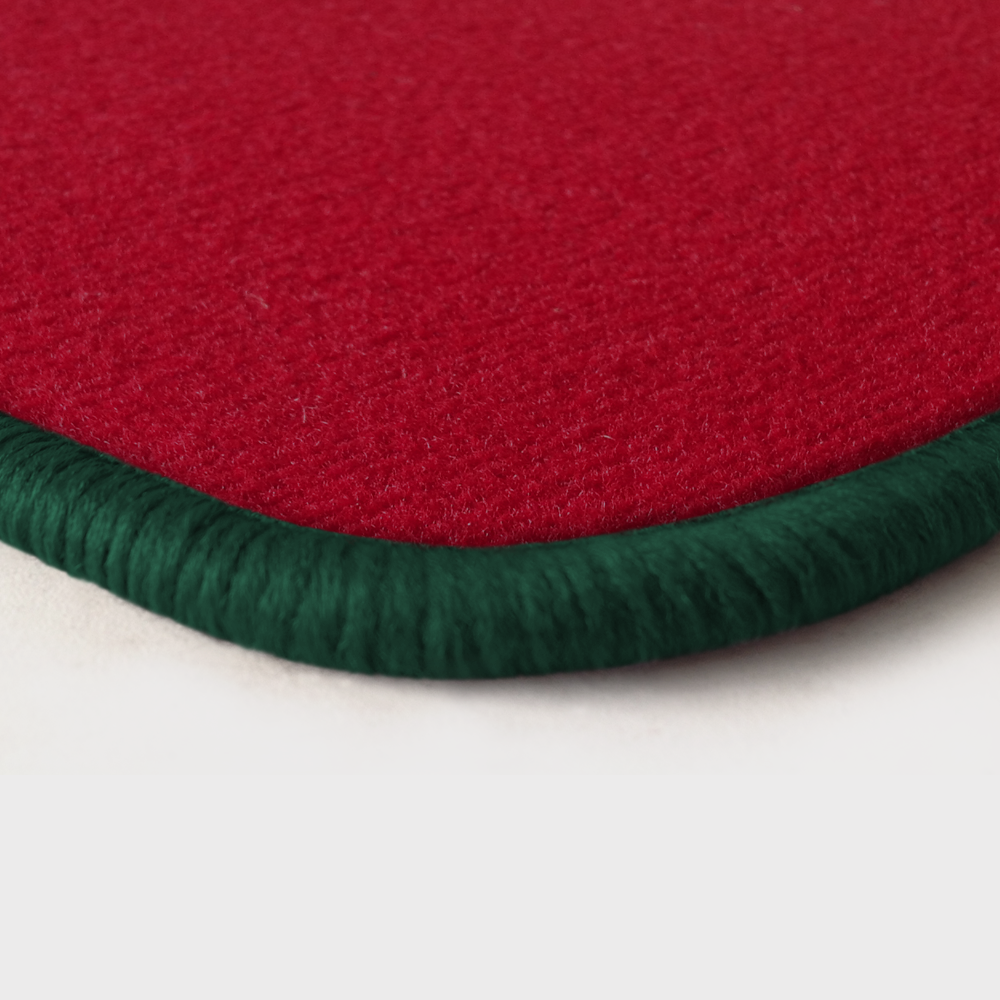 Eine Ecke als Beispiel einer Fussmatte Velours rot mit Rand in dunkelgruen.