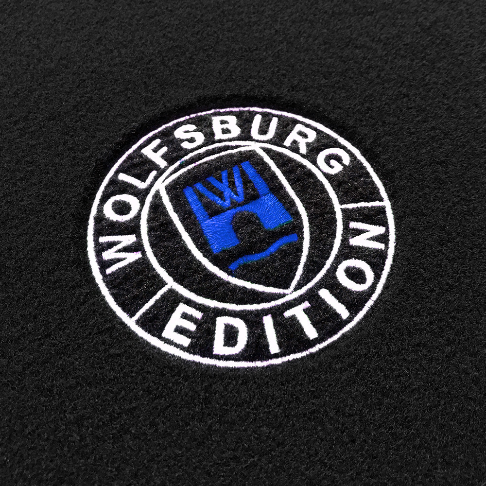 wob Stick Detail-204 royalblau Das gestickte Wolfsburg Editions Logo auf einem schwarzen Teppich und das Logo ist in royalblau.