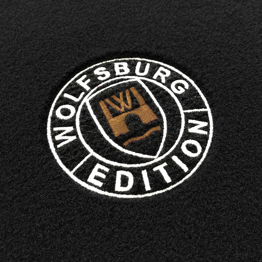 Das gestickte Wolfsburg Editions Logo auf einem schwarzen Teppich und das Logo ist in beige.
