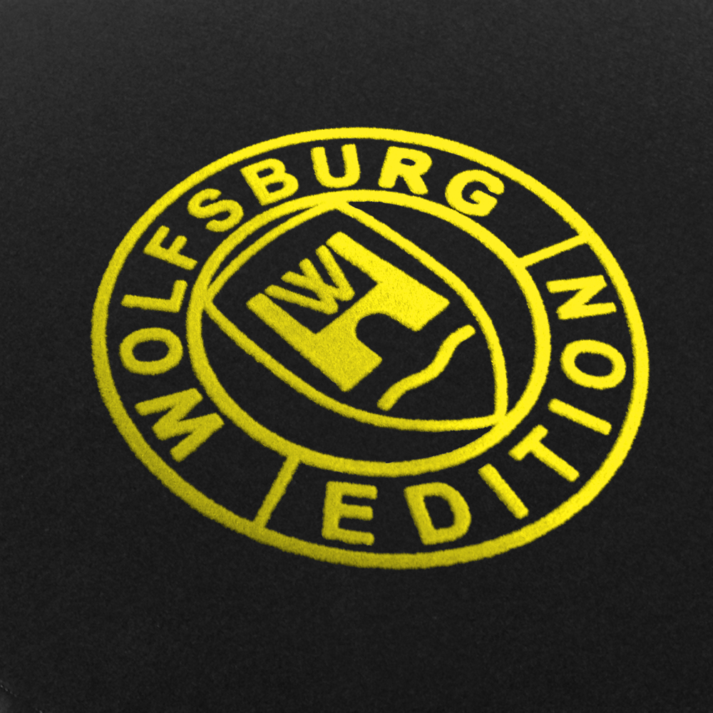 WOB Detail-201-gelb Das Wolfsburg Editions Logo auf einem schwarzen Teppich und das Logo ist in gelb.
